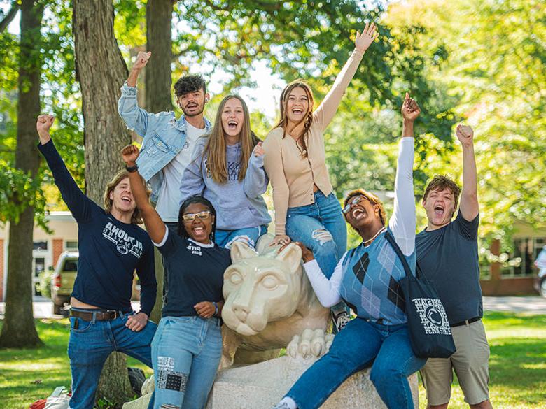 Students cheering while sitting on the Lion Shrine statue